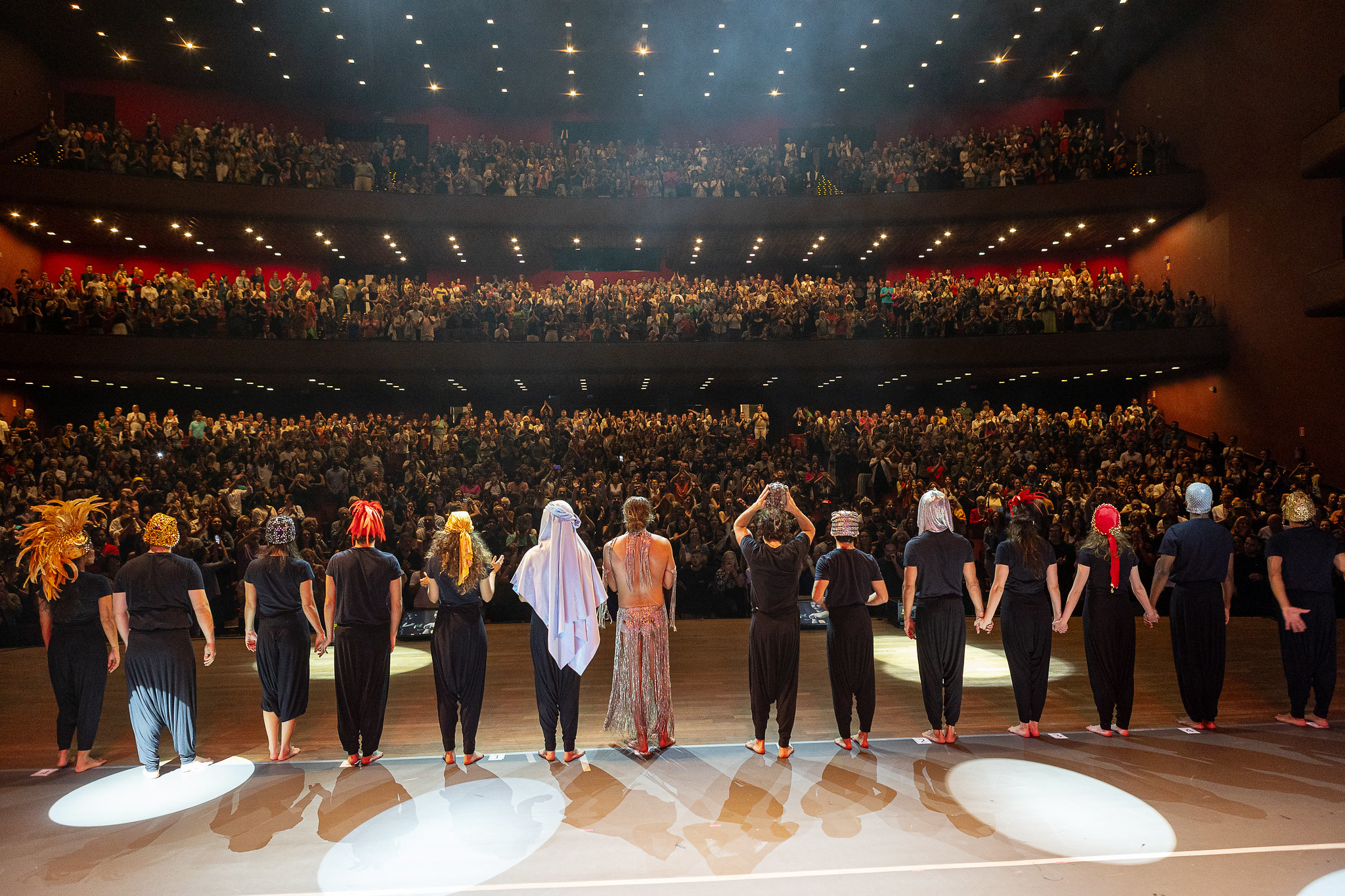 Imagem das costas de atores no palco mostrando o público em um teatro